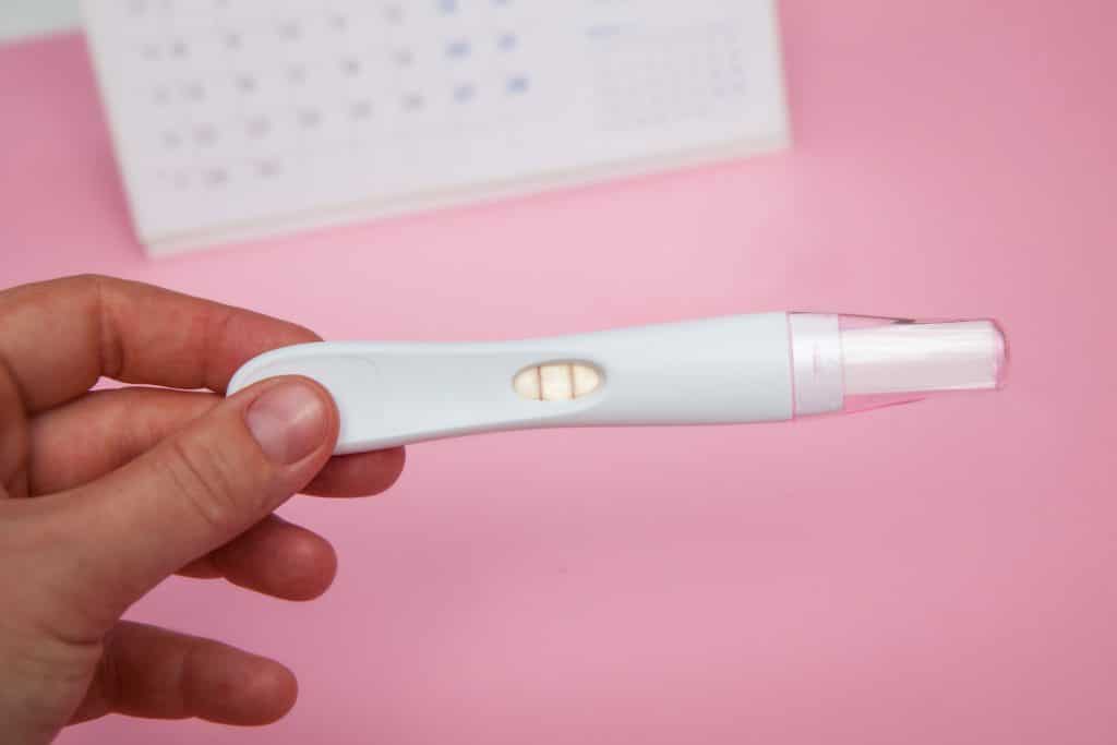 hand holding pregnancy test on pink background