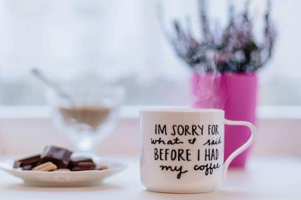 mug that reads 'I'm sorry for what I said before I had my coffee'. There's a vase of flowers and plate of chocolate.