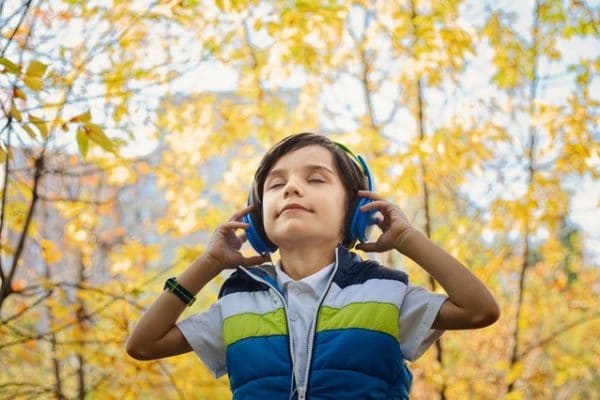 Boy listening to headphones outside in front of a fall tree