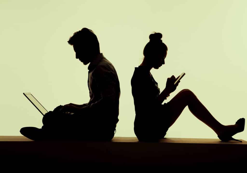 silhouette of man and woman on devices with backs to each other