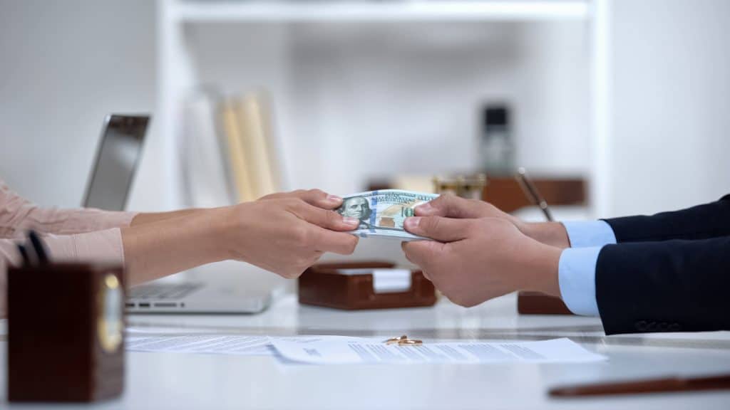 man's and woman's hands pulling at $100 bill across desk