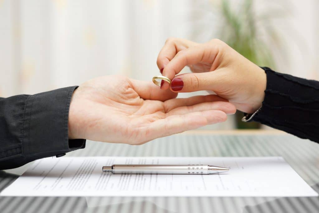 Woman's hand putting wedding ring into man's hand over divorce paperwork