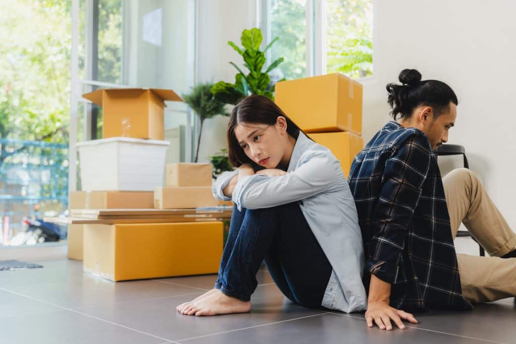 sad couple sitting on floor surrounded by cardboard moving boxes