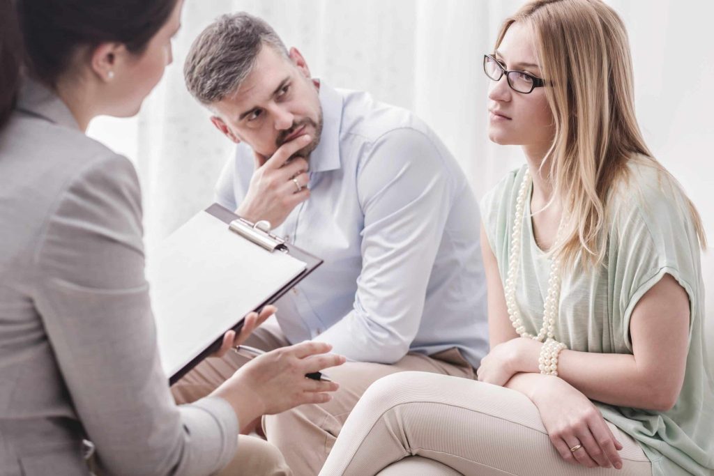 A husband and wife sitting on a couch talking to a family mediator.