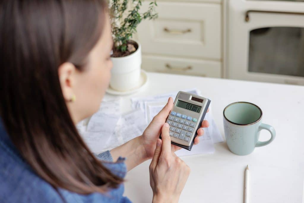 woman using calculator while sitting in kitchen