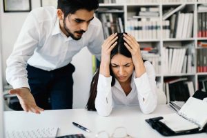 A businessman yells at his coworkers as she sits at her desk