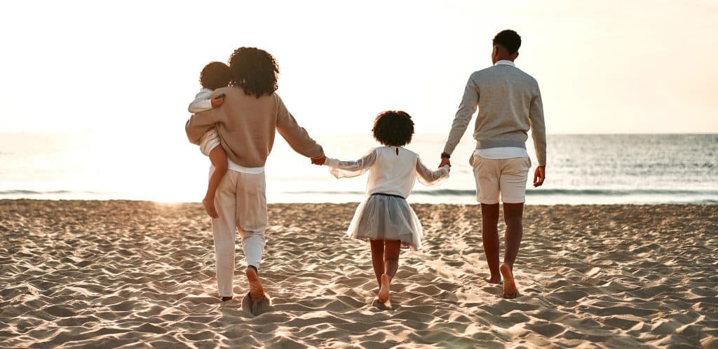 girl holding hands with her parents on a beach