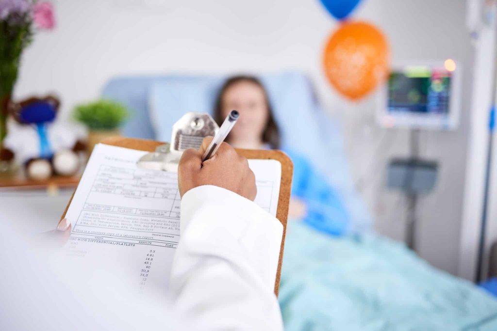 Doctor filling out paperwork with blurred woman in hospital bed